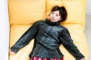 黄色のソファに寝転がり考え事をしている黒のセーターを着た女性